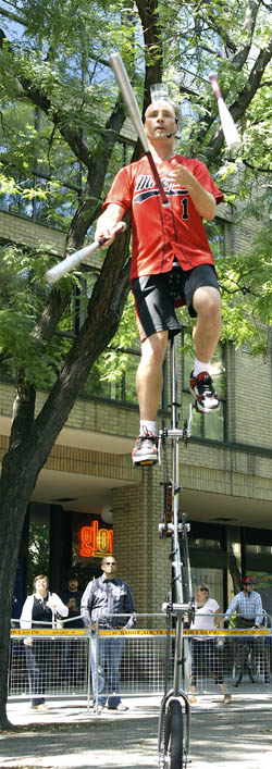 来自澳大利亚的Spin先生在Unicycle上杂耍蝙蝠，同时在多伦多Buskerfest开球时在头上平衡一杯水
